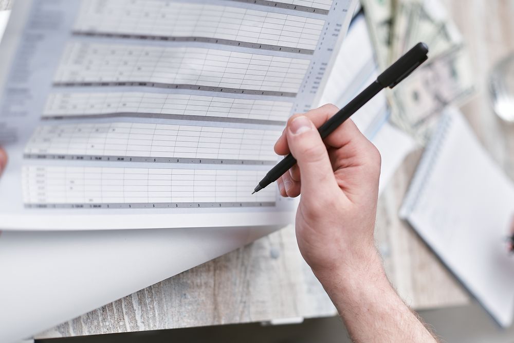 Hand with a pen going through a budget sheet